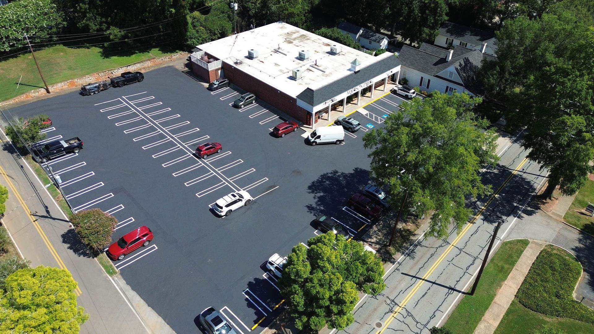 Aerial view of a parking lot and a brick building with a white roof. Several cars are parked.