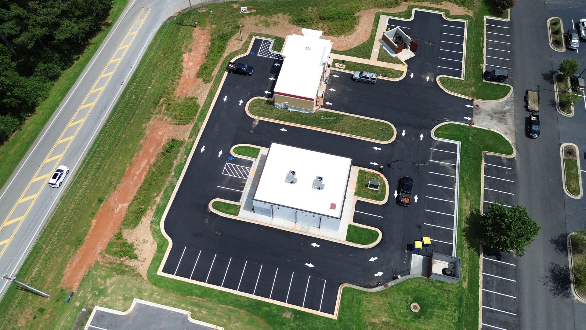 Aerial view of a commercial building with parking, adjacent to a road with a grassy median and trees.