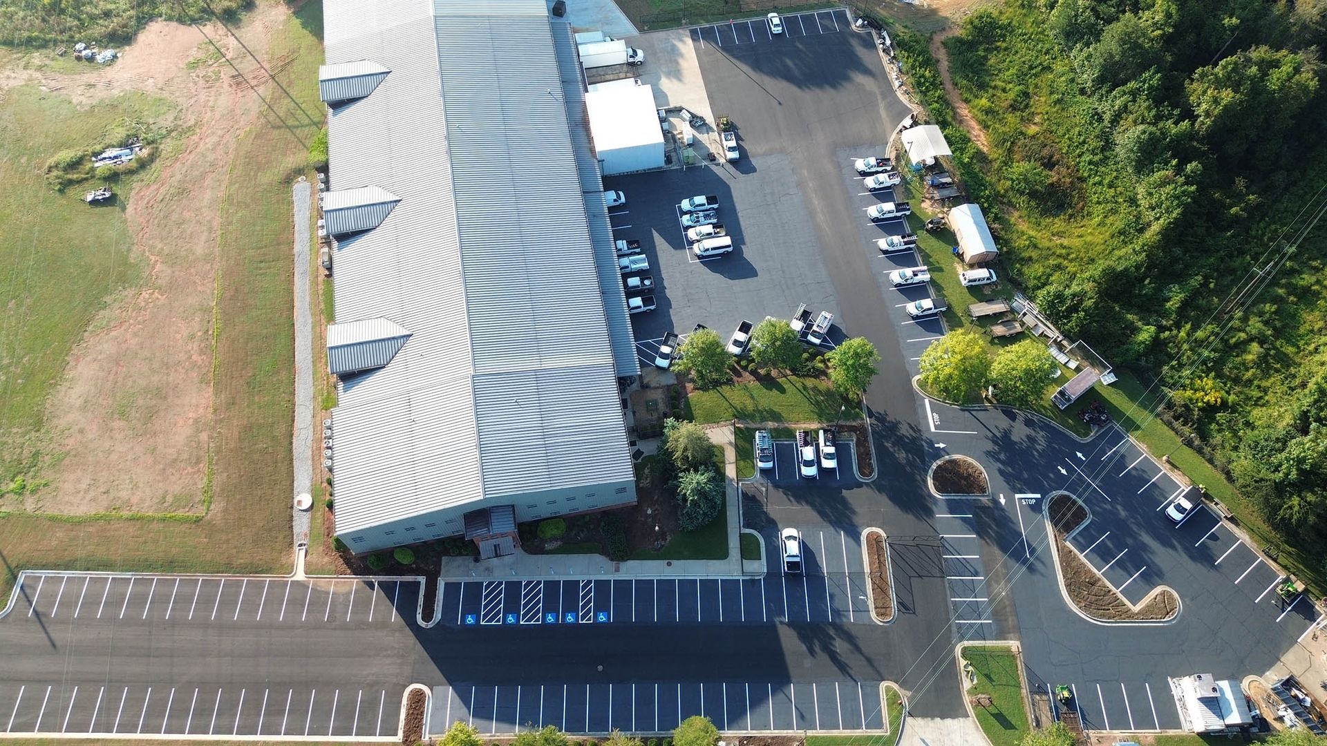 Aerial view of a large industrial building with a parking lot filled with cars and a patch of green landscaping.