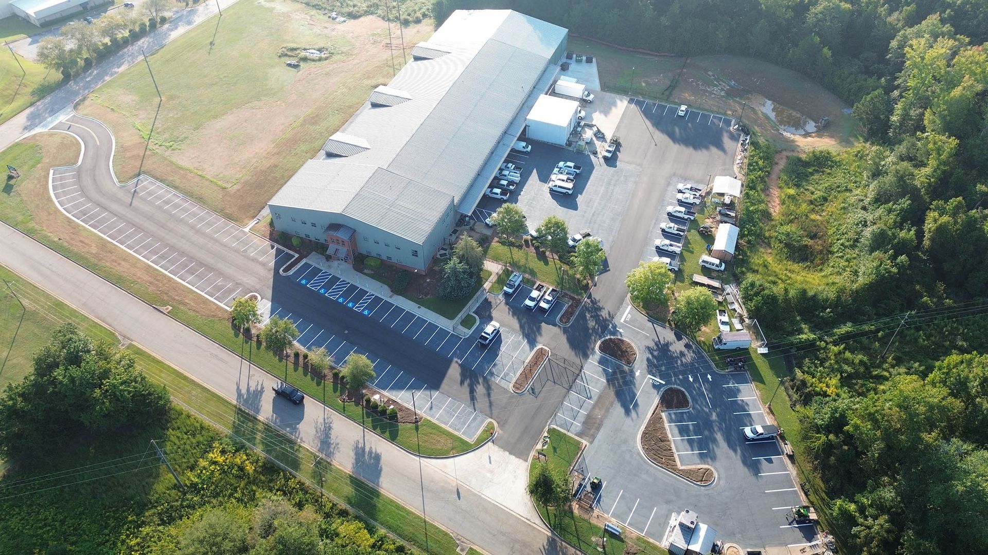 Aerial view of a large industrial building with a parking lot and surrounding trees.