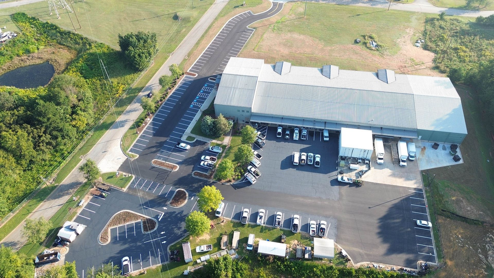 Aerial view of a large industrial building with loading docks, surrounded by parking and greenery.