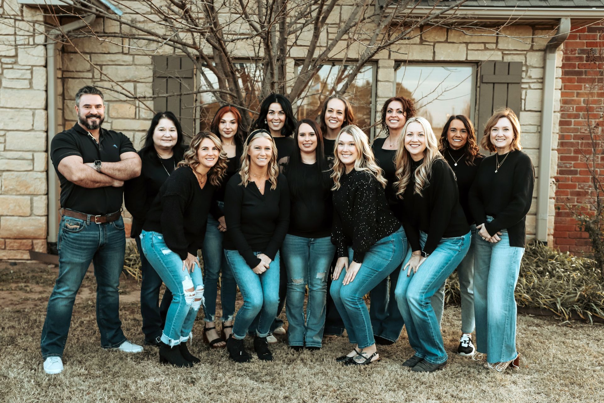 Group of people wearing black tops and jeans posing in front of a stone building.