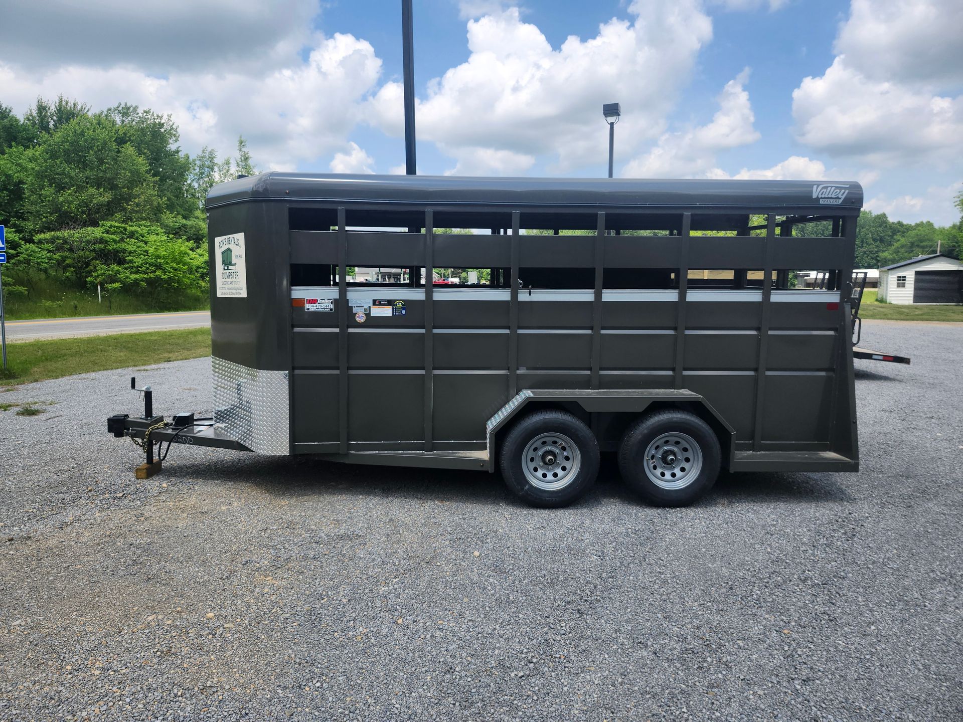 Dark gray livestock trailer parked on gravel, with a blue sky background.