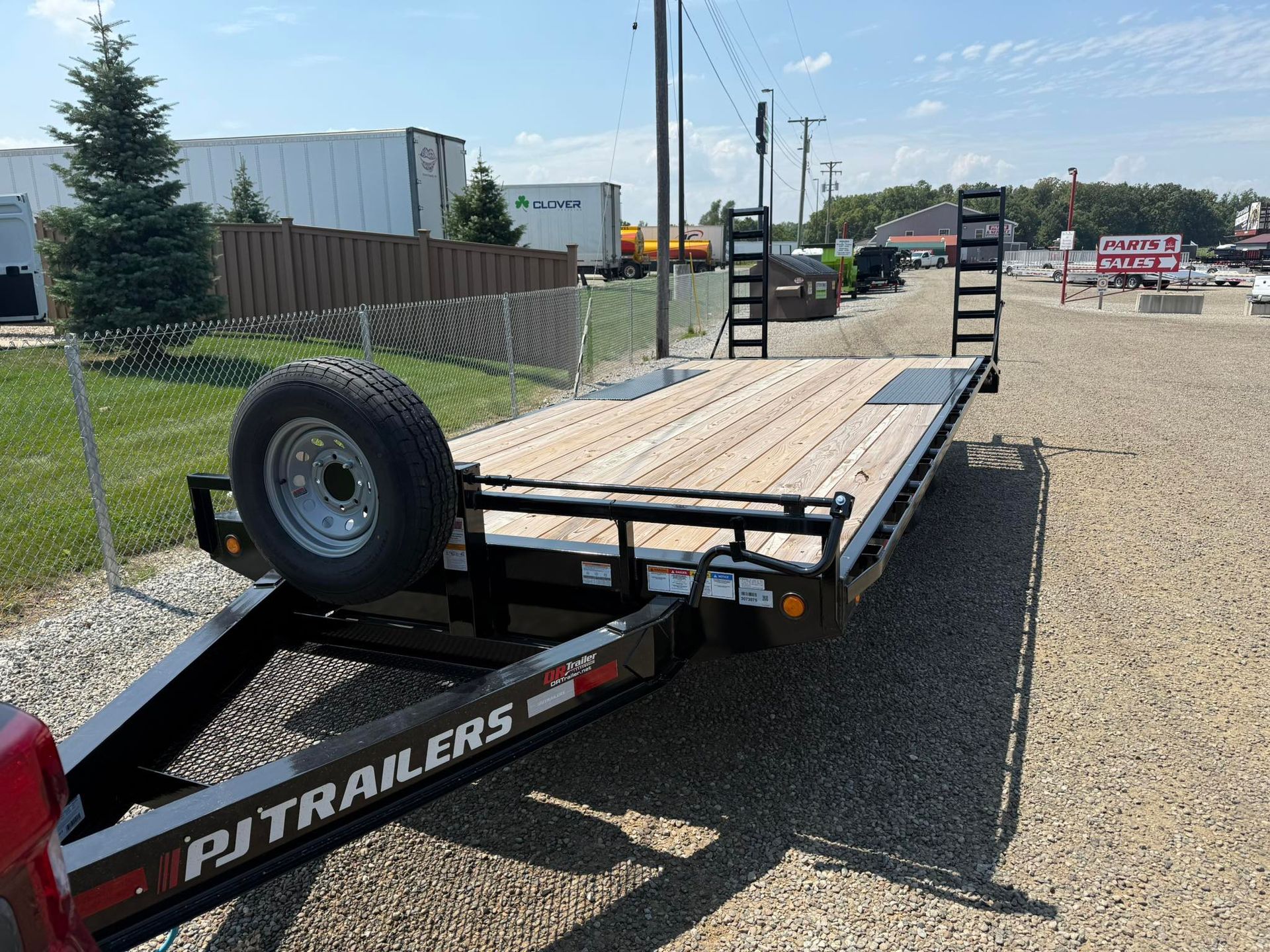 Black flatbed trailer with wooden deck on gravel, sunny day.