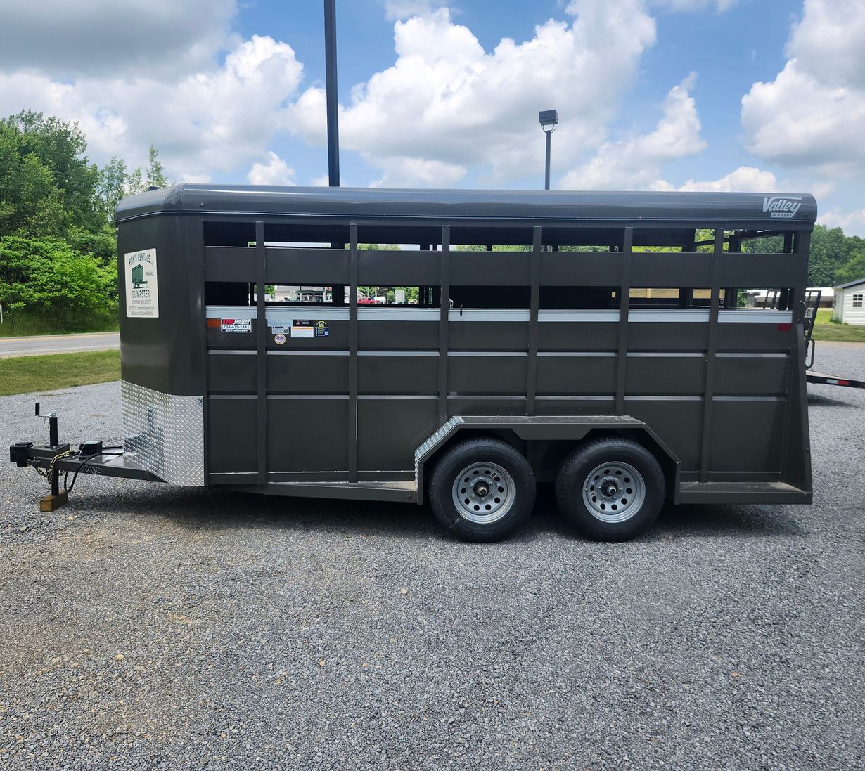 Dark gray livestock trailer on gravel, with two axles and a hitch.