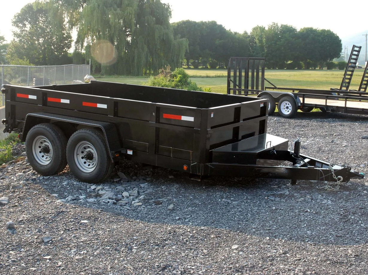 Black utility trailer with dual wheels, parked on gravel.