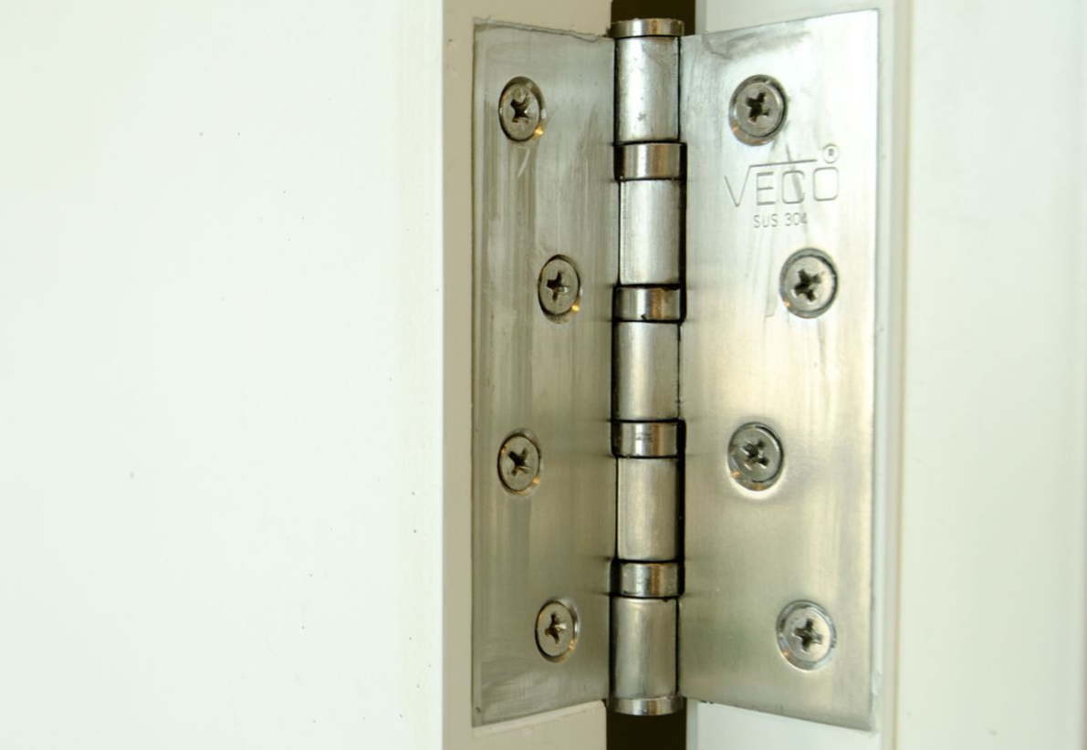 Silver door hinge attached to a white door and frame.