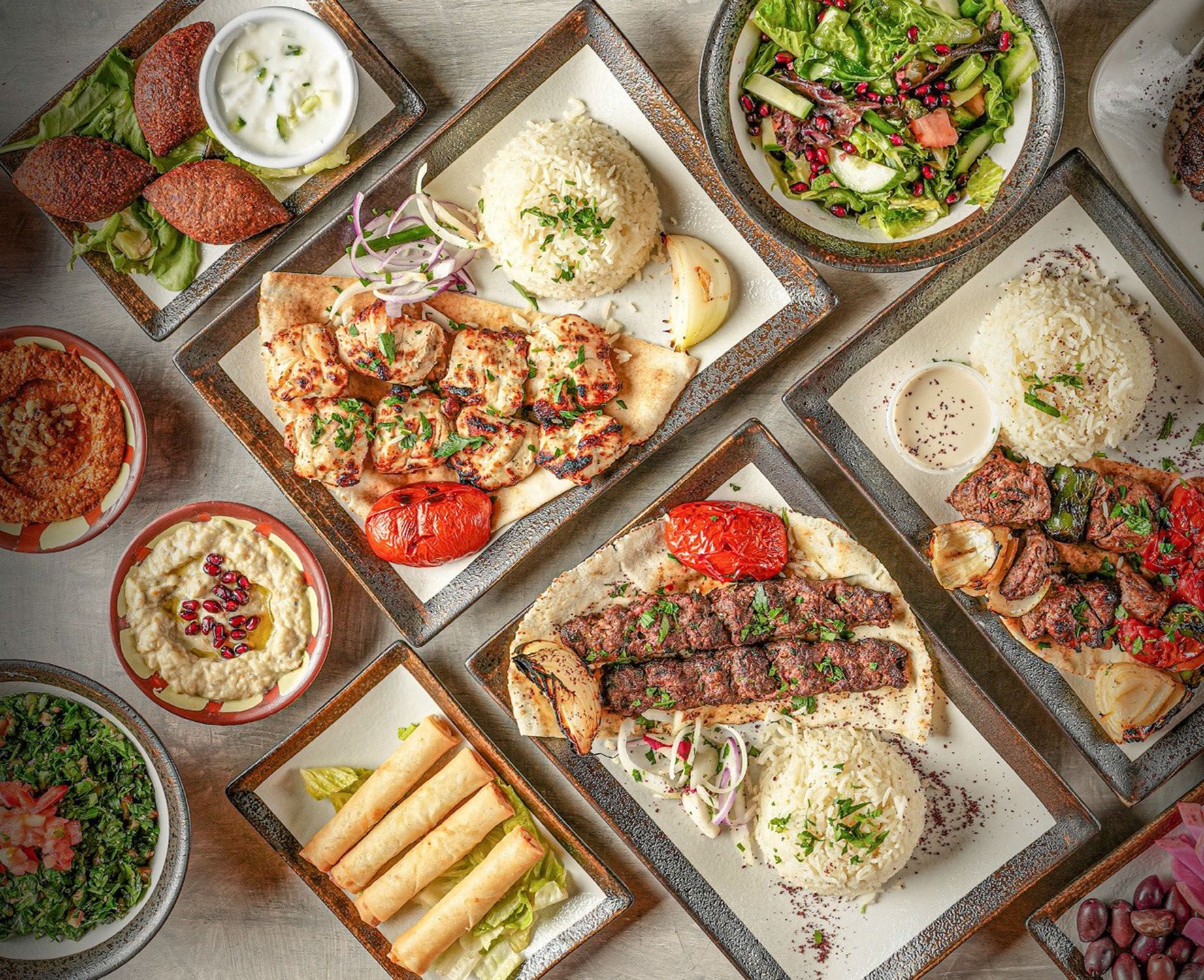 Overhead shot of Lebanese dishes on plates: kebabs, rice, salad, hummus, and appetizers.
