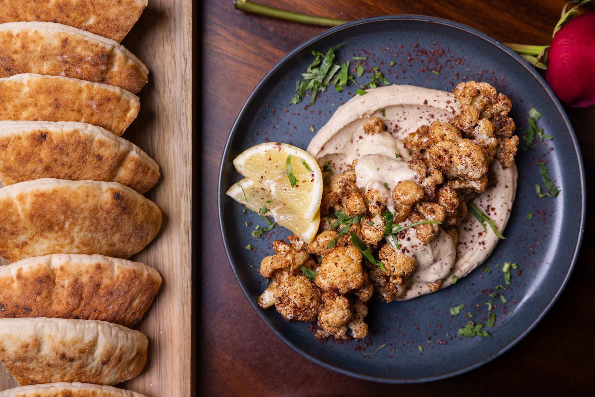 Hummus topped with roasted cauliflower, lemon slice, and pita bread.