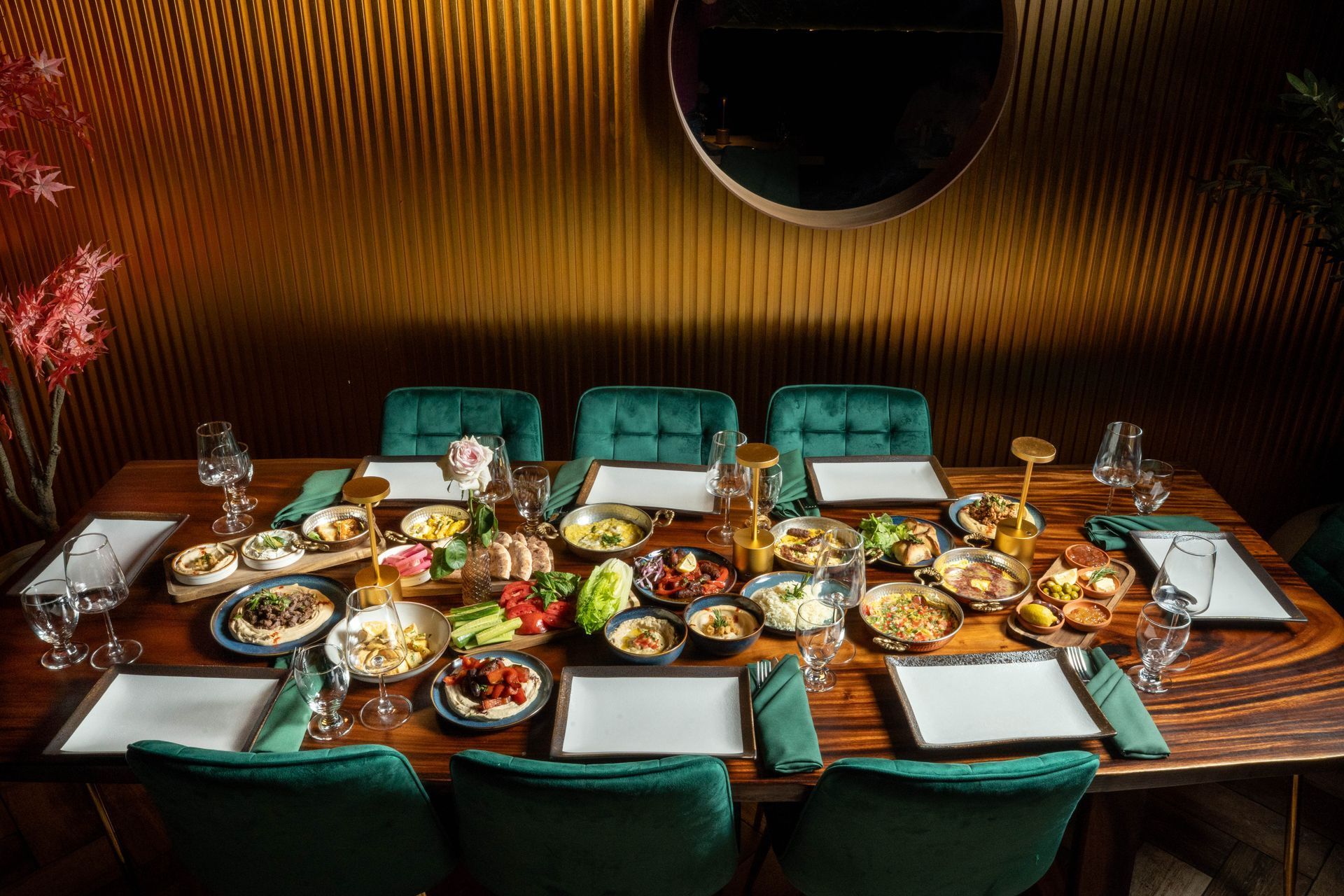 Formal dining table set with various Middle Eastern dishes, green chairs, and golden wall.