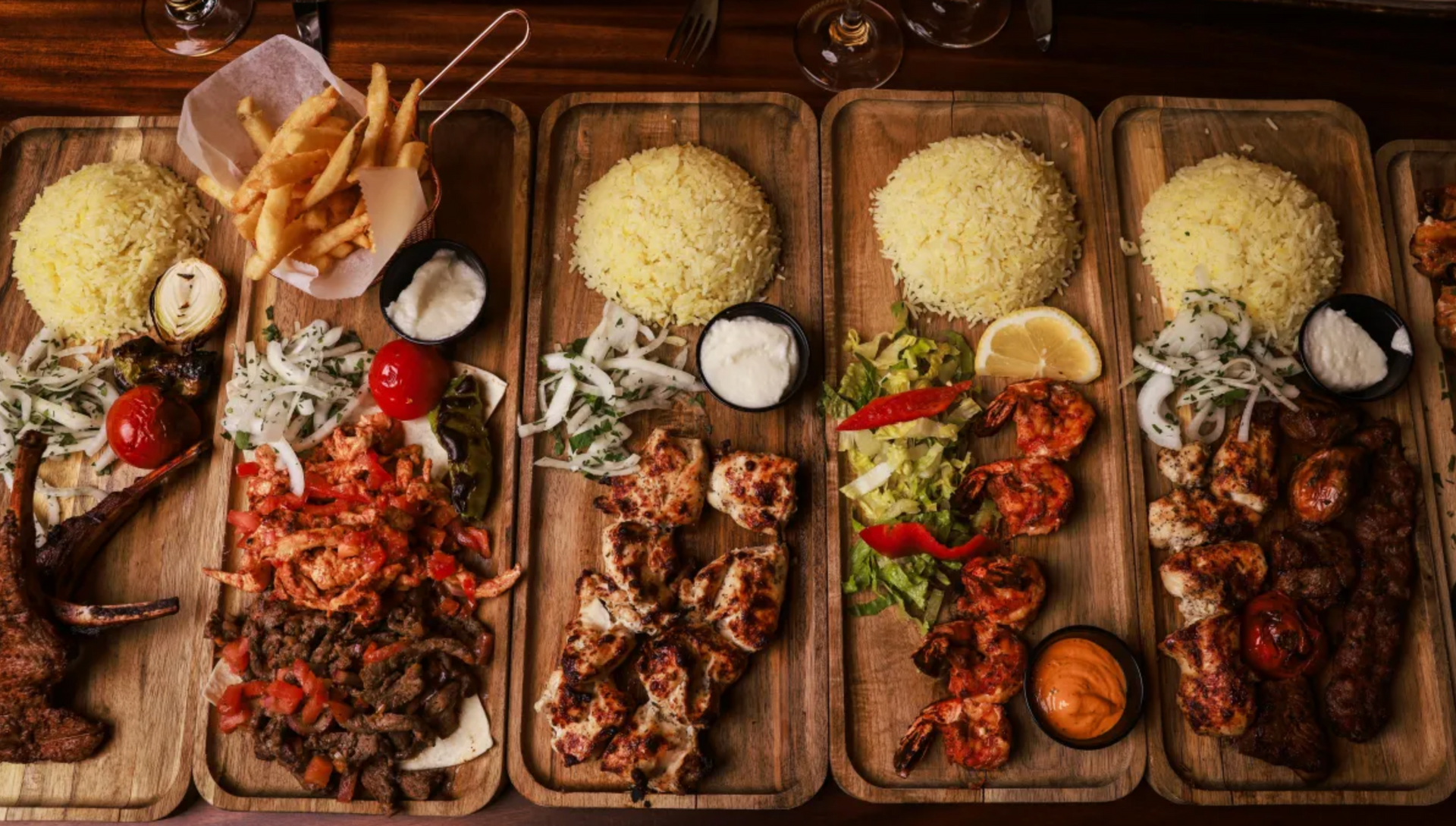 Four platters of grilled meat and rice with garnishes and dipping sauces.