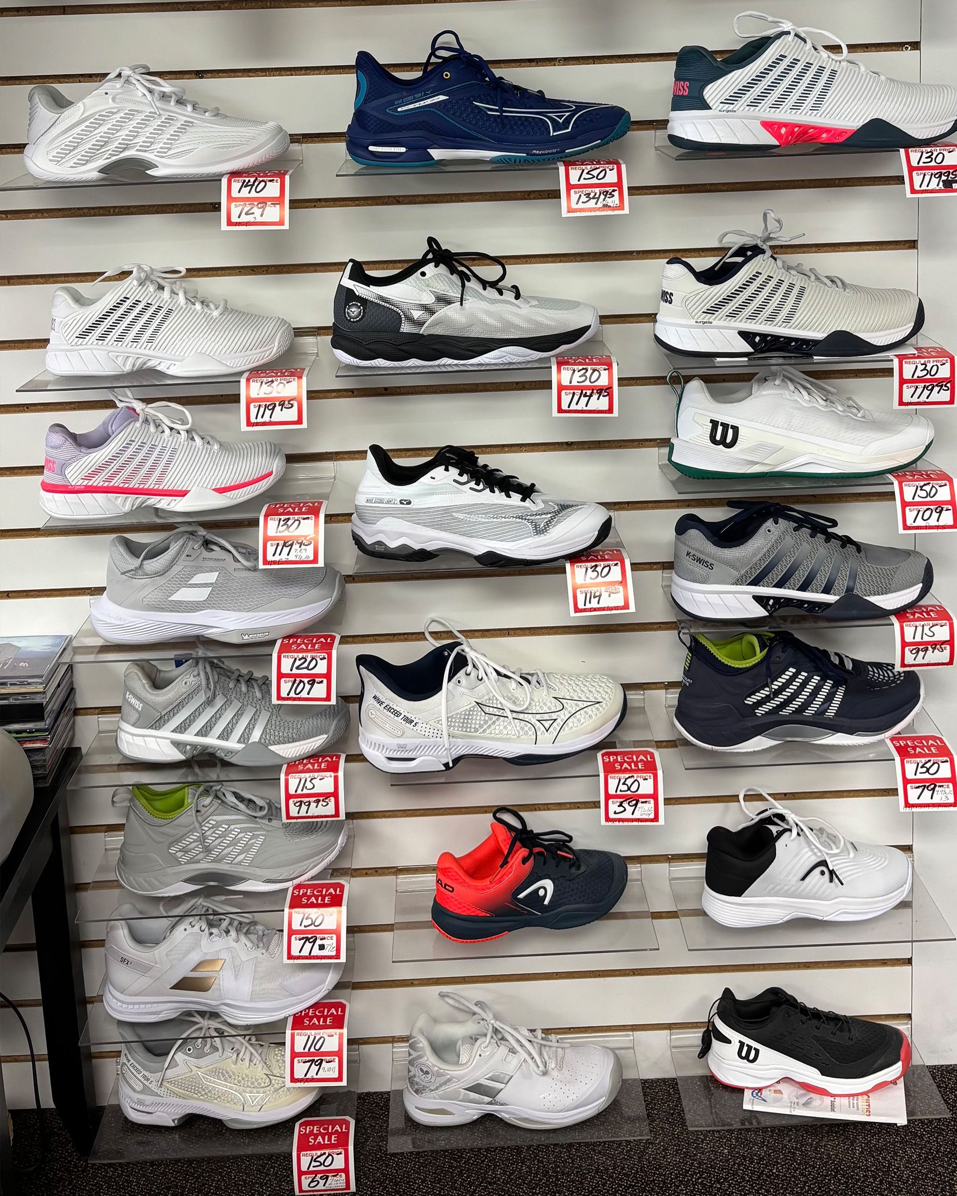A wall display of various athletic tennis shoes arranged in rows with price tags attached to the shelves.