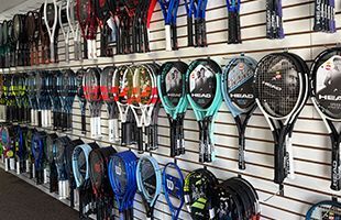 A wall display featuring rows of various colorful tennis racquets, including many branded HEAD racquets.