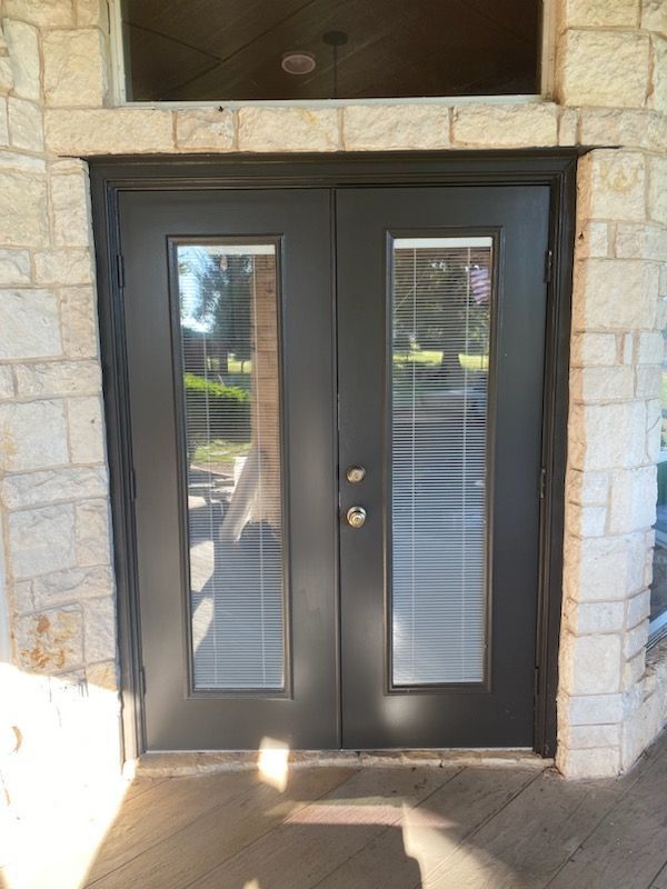 A black door with blinds on it is on a brick building.