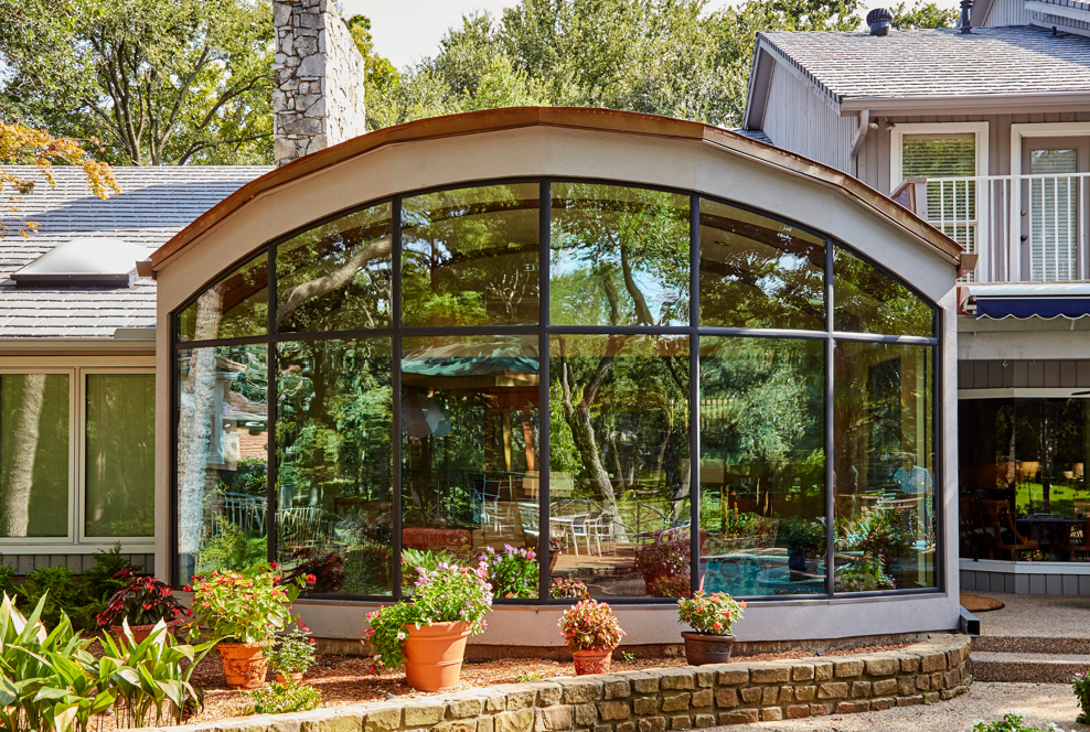 a house with a large sunroom with lots of windows and potted plants in front of it