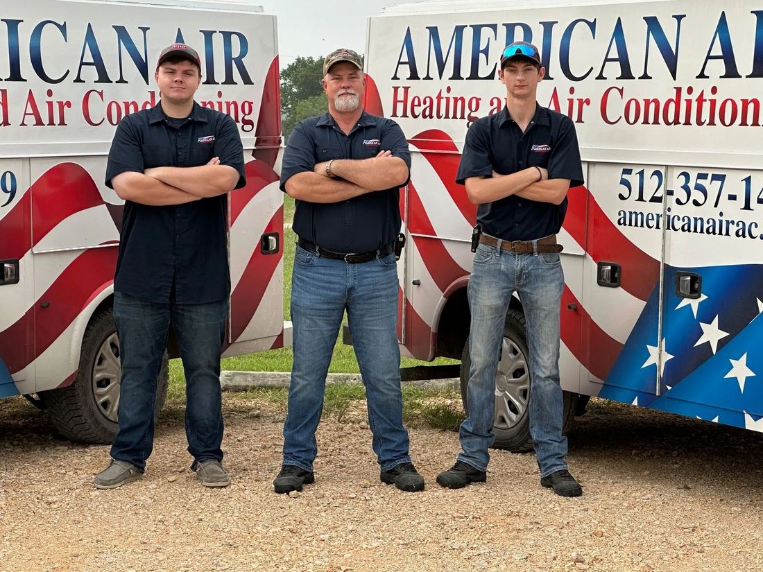 Three men standing in front of two American air conditioning trucks