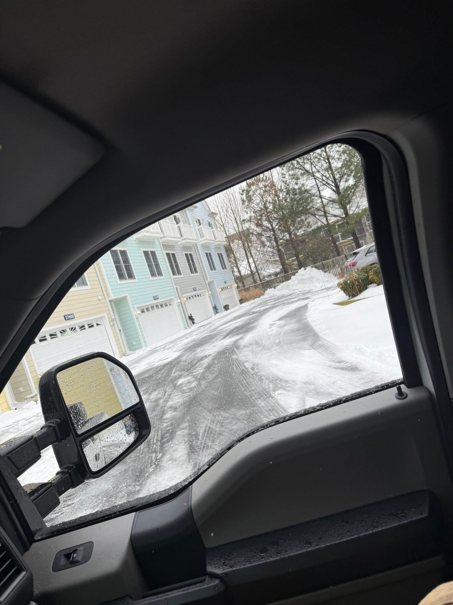 View from inside a car window, snow-covered road, and buildings are visible.