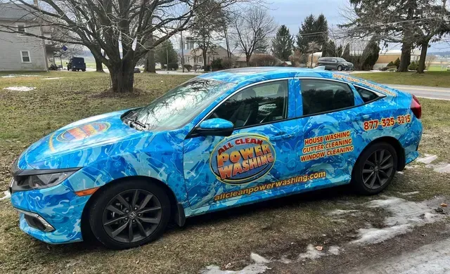 A blue patterned Honda sedan parked on grass, branded with “All Clean Power Washing” and contact information on the side.