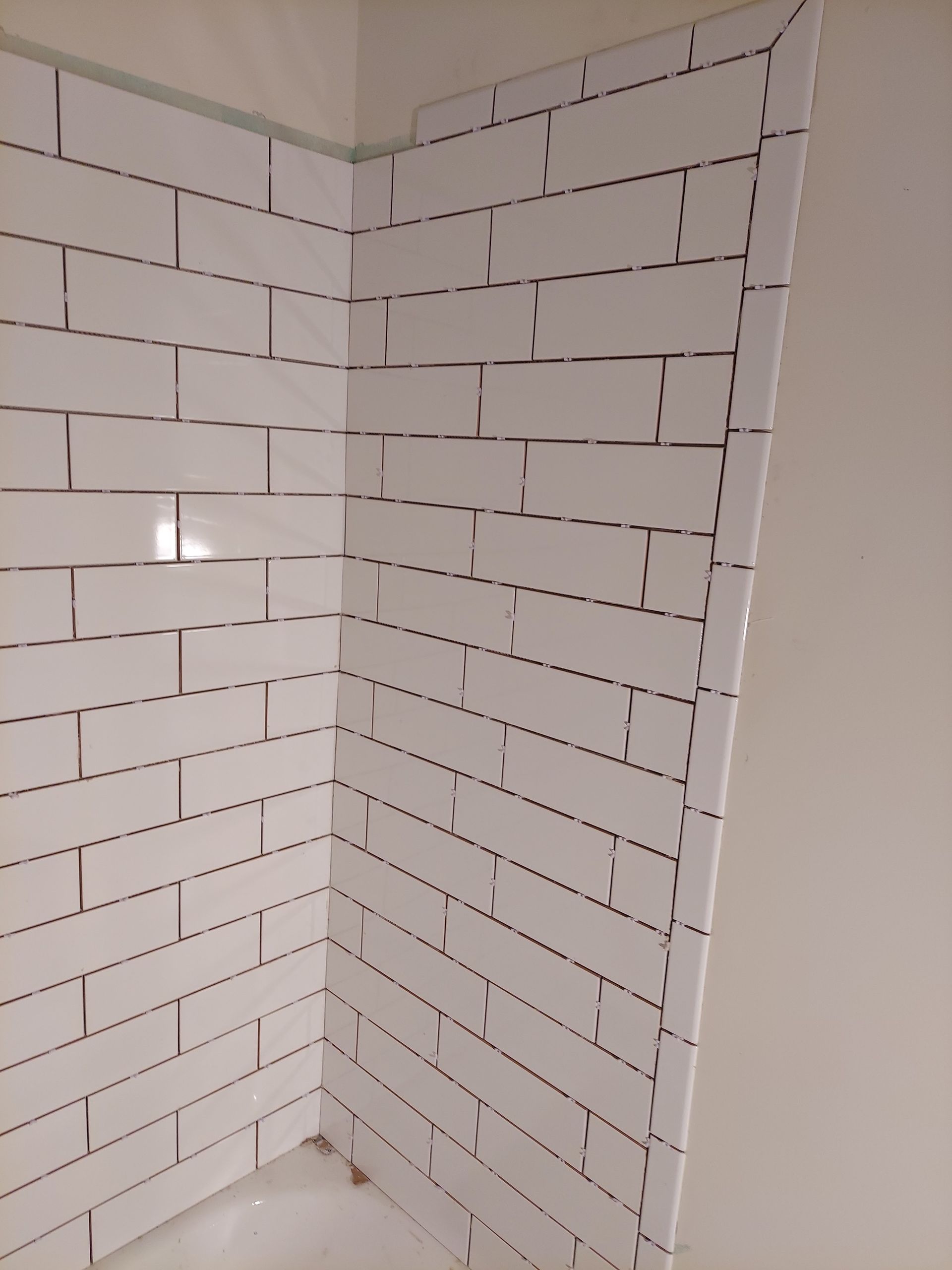 A corner view of a shower wall covered in white subway tiles, with an uneven, unfinished edge along the right side.