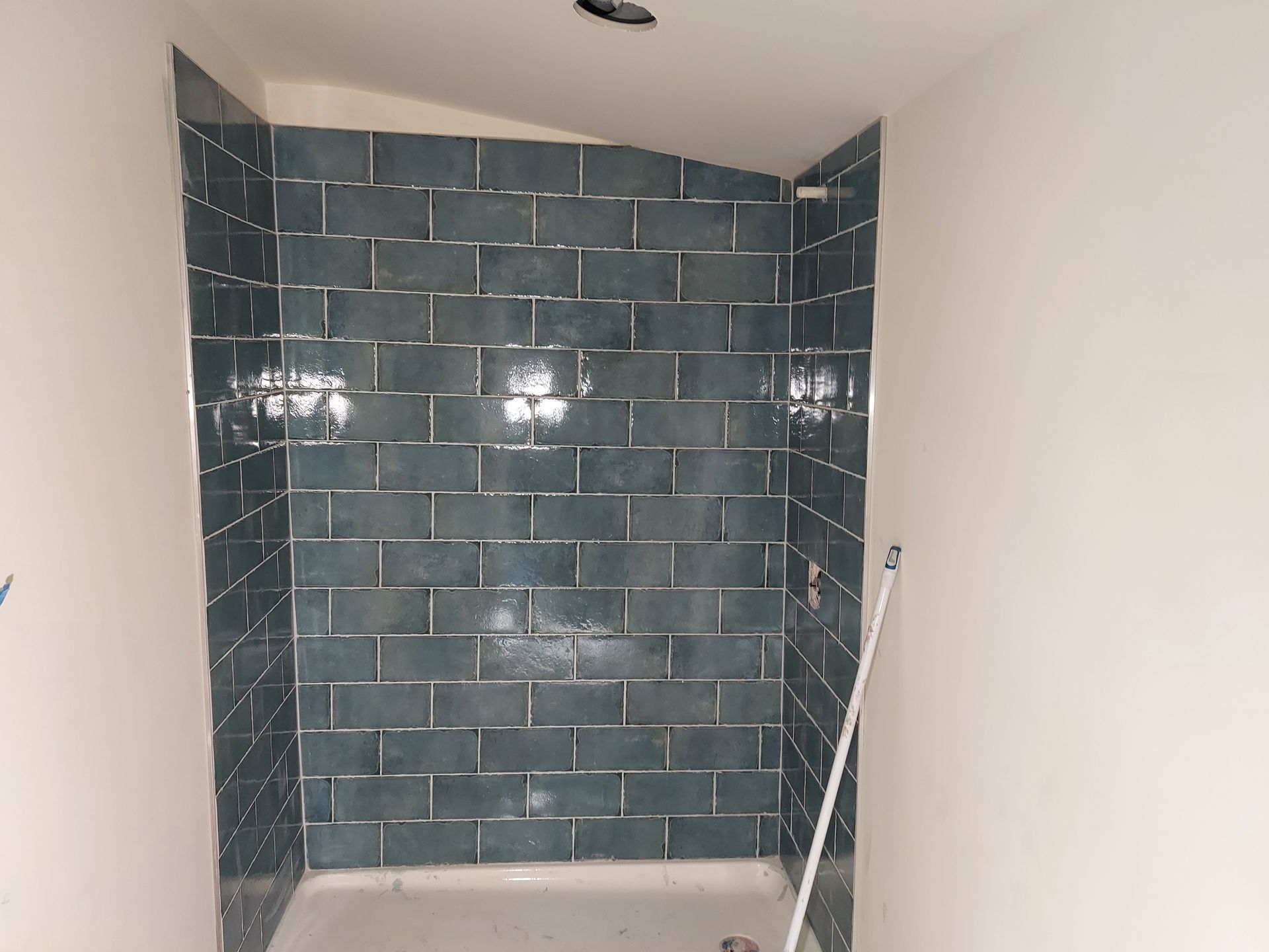 A shower stall with dark blue subway-style wall tiles and a white base, seen from a slightly elevated angle.