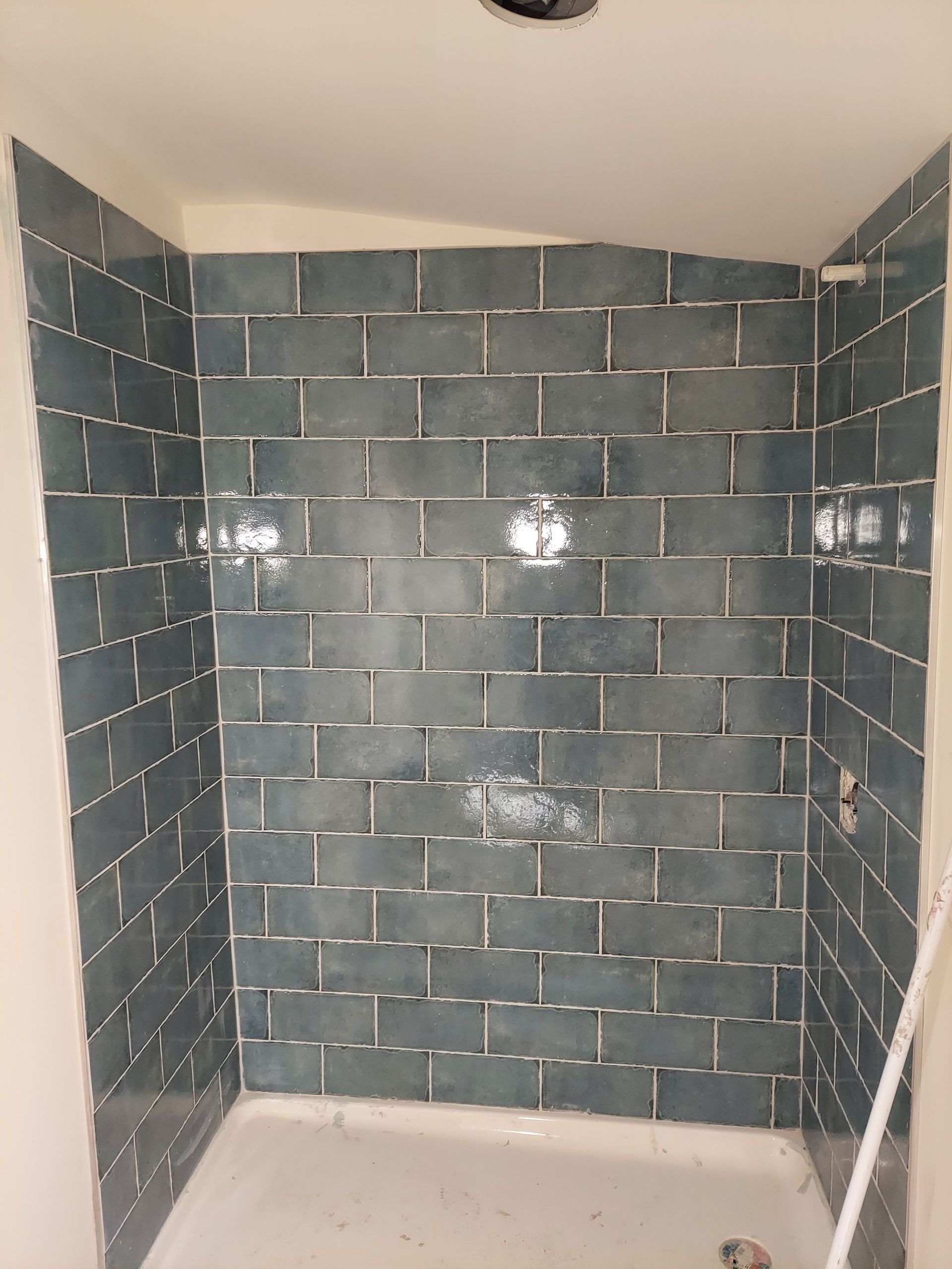 A shower stall featuring blue subway tiles installed on the back and side walls above a white base.