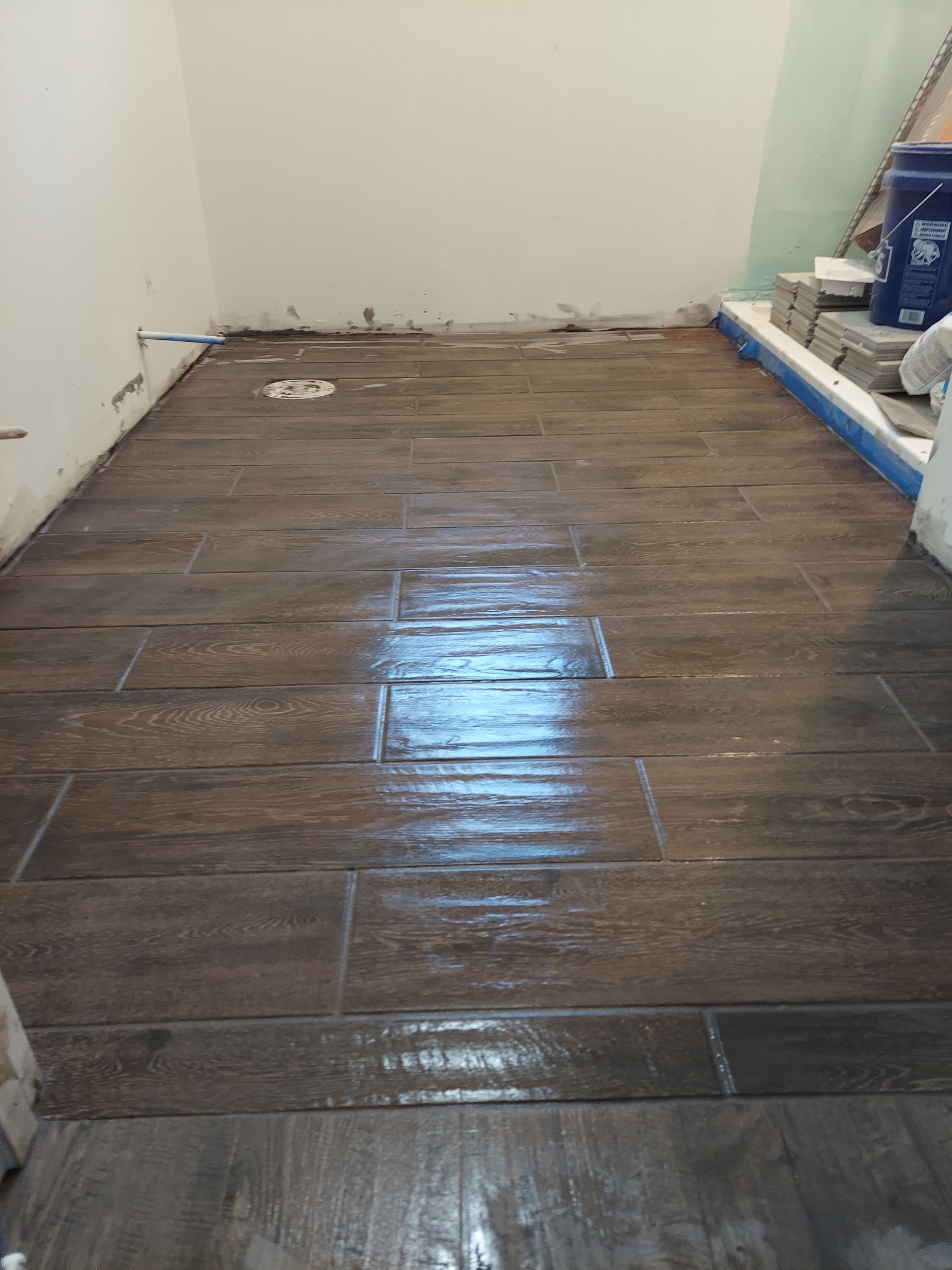 A room with freshly installed brown wood-look floor tiles and a wet, glossy finish.