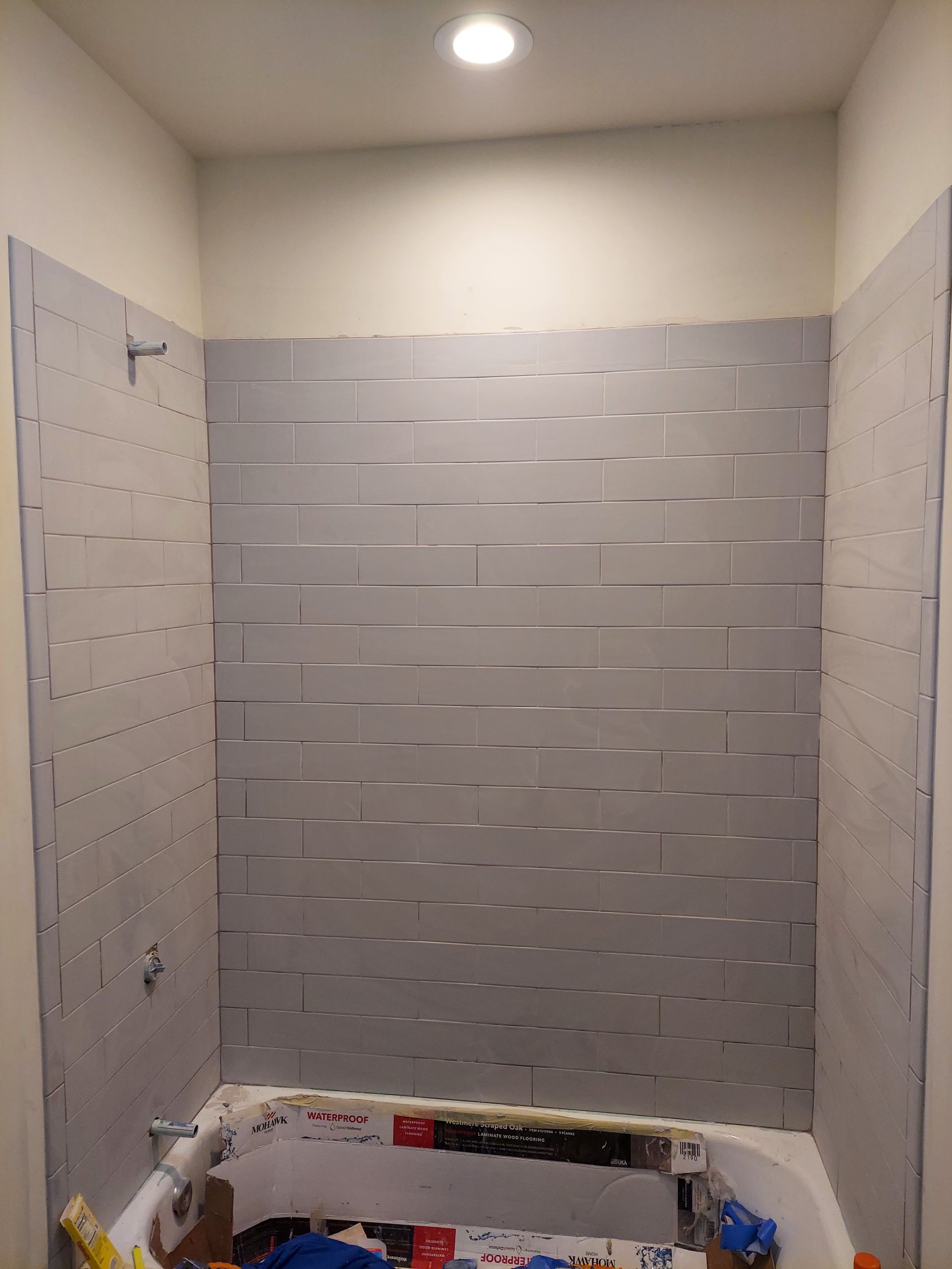 A bathtub surround under renovation, featuring gray, horizontal foam-style insulation panels mounted on the shower walls.