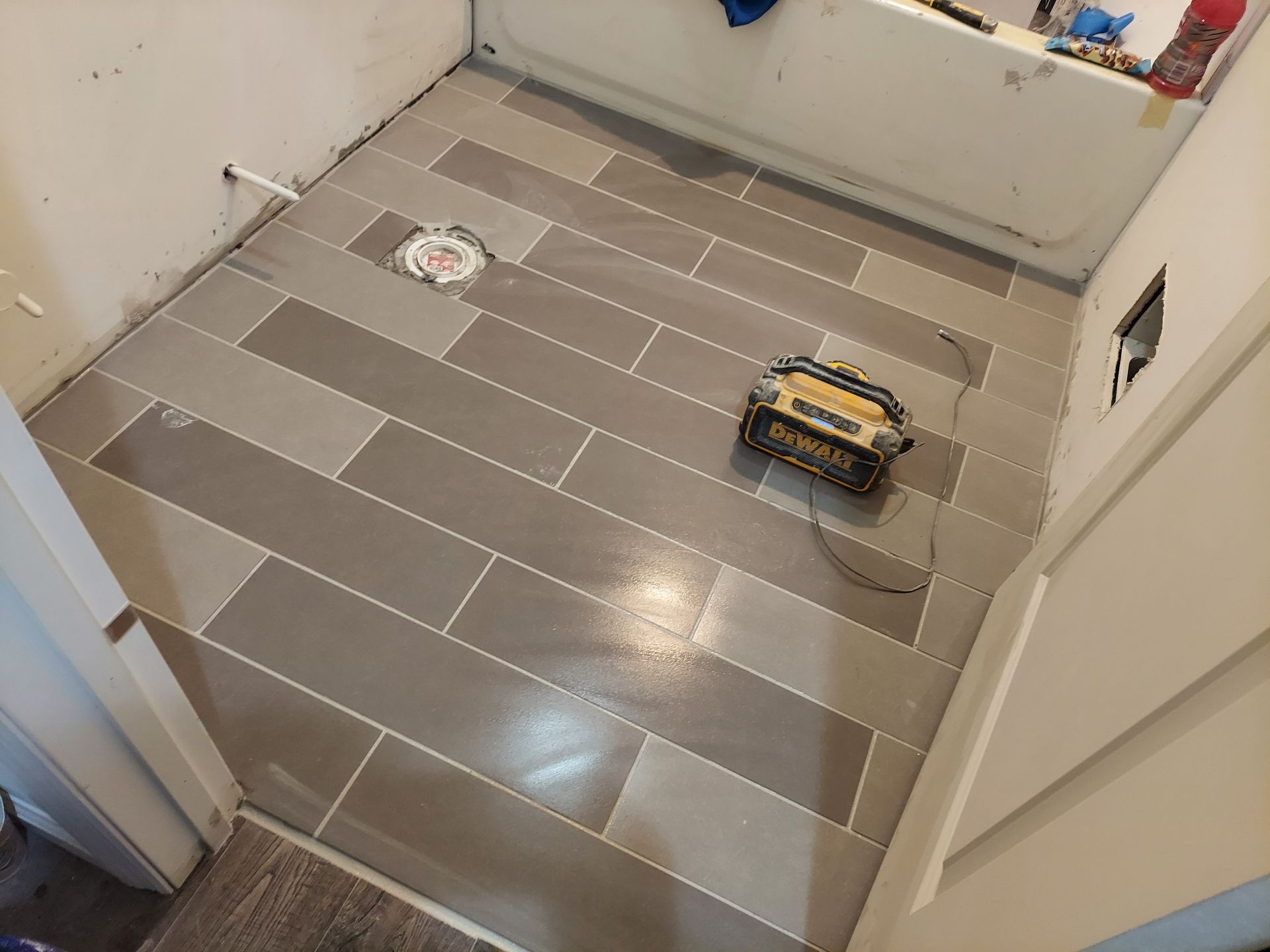 A recently tiled bathroom floor with gray rectangular tiles, a central toilet flange, and a small tool case on the floor.