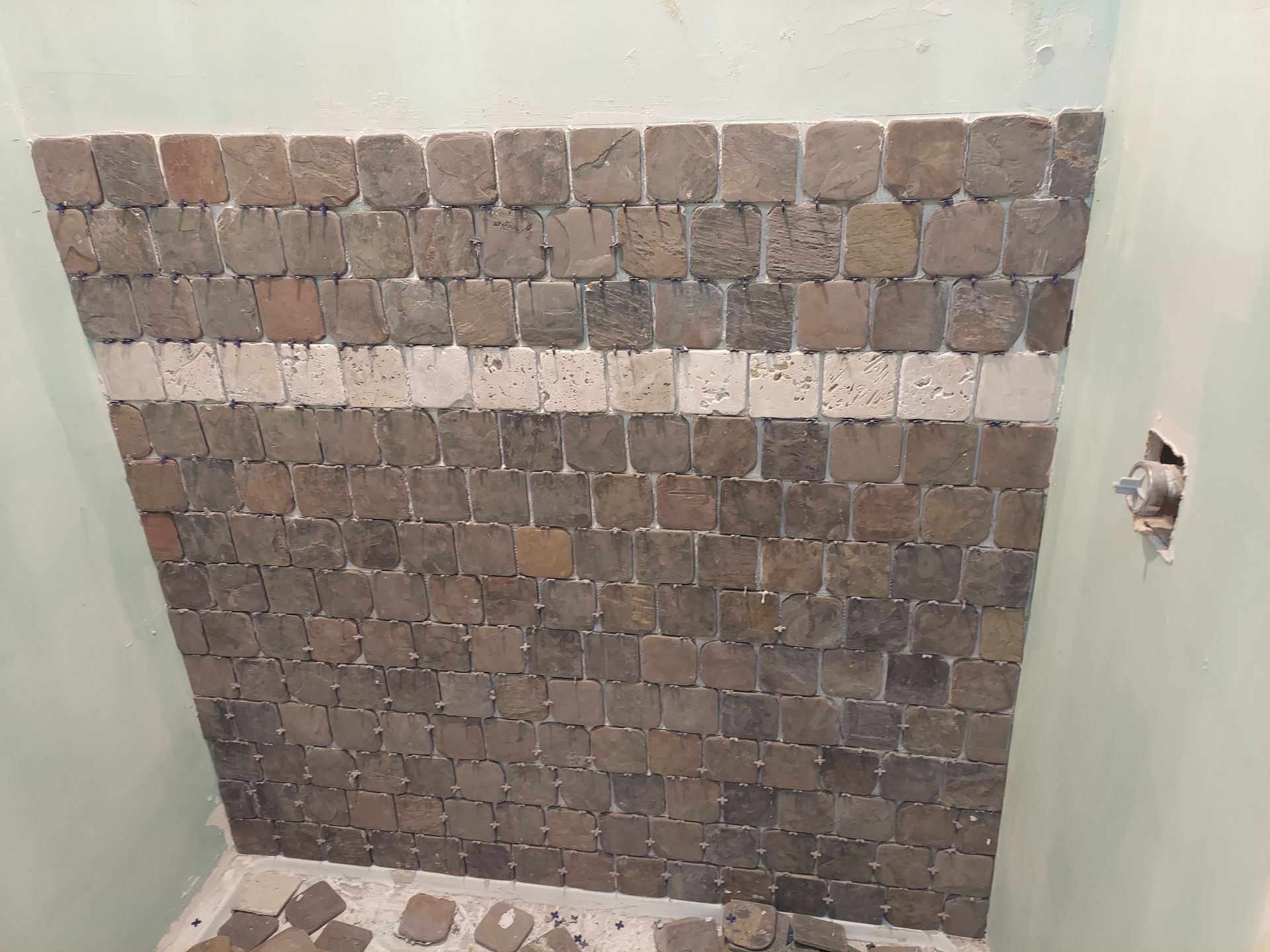 A partially tiled wall with dark square tiles and a single horizontal row of light-colored tiles in the middle.