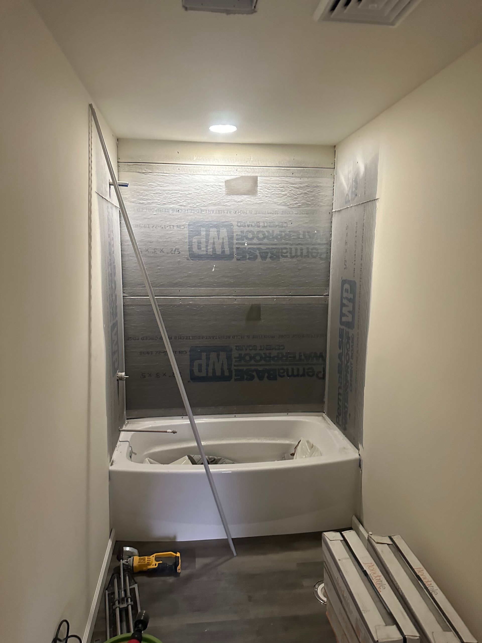 A bathroom under renovation featuring a white bathtub surrounded by gray waterproof backing material on the walls.