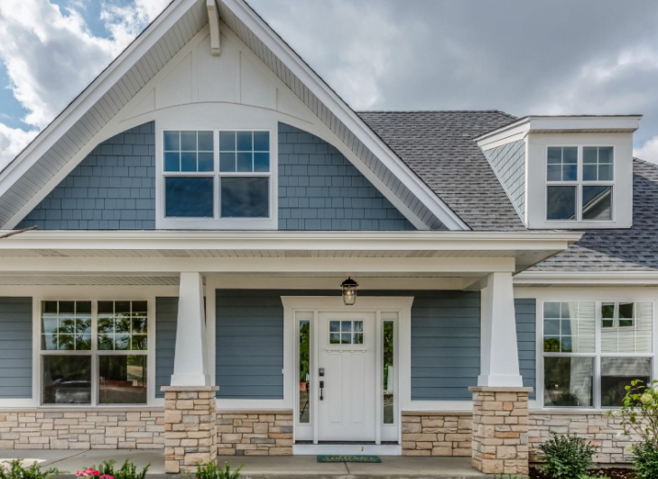 A blue-sided cottage house with a white front door, stone accents on the lower walls, and a large porch.