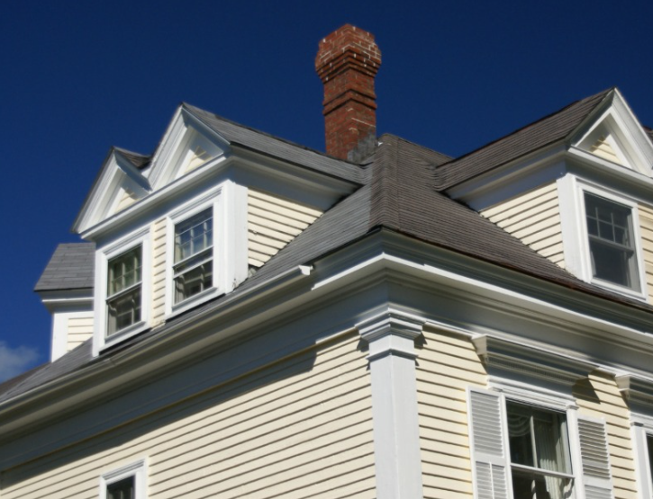 Light yellow house with white trim, two gabled dormer windows, and a brick chimney against a deep blue sky.