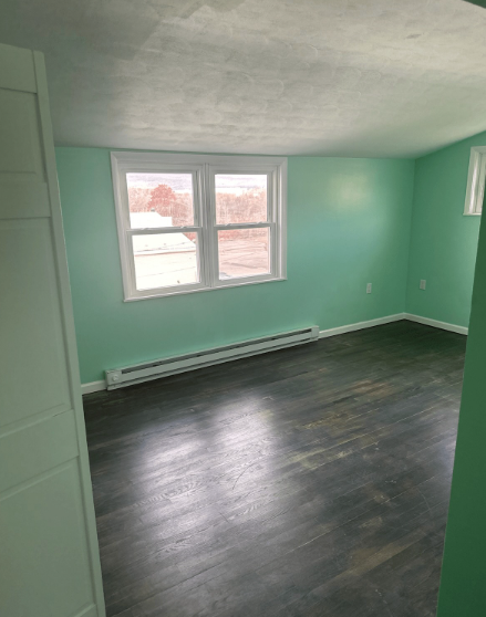 An empty room with mint green walls, dark wood floors, and a double-hung window on the far wall.