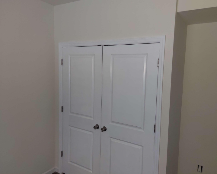 White double interior closet doors with rectangular panels and metal knobs installed in a beige room.