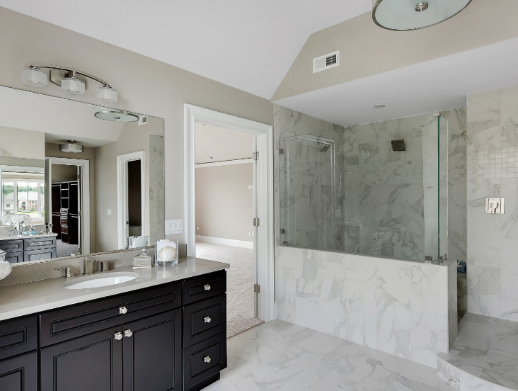 Modern bathroom with a dark wood vanity, white marble floors, and a glass-enclosed walk-in shower.