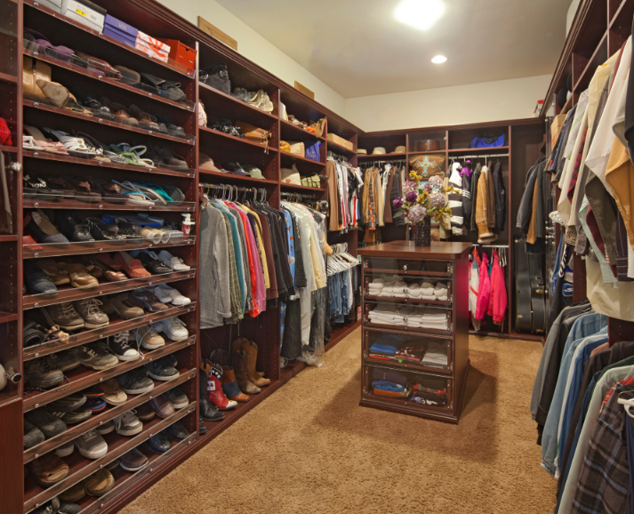 A spacious, organized walk-in closet with dark wood shelving, numerous shoes, hanging clothes, and a central island unit.