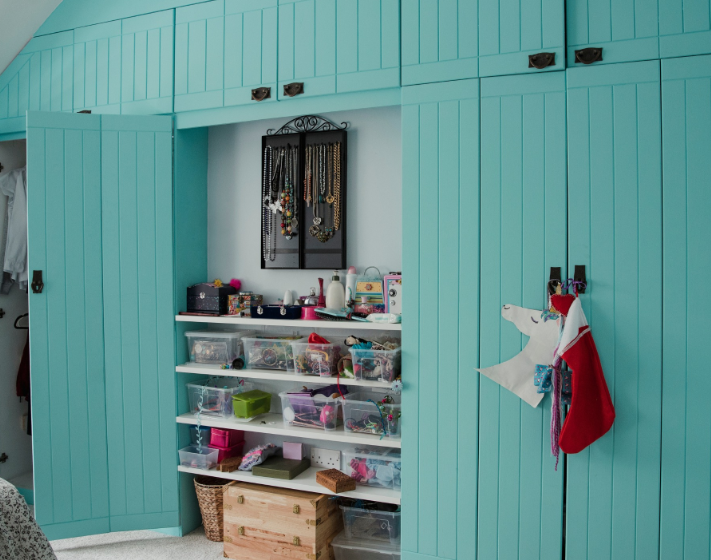 Bright teal storage cabinets flank a center shelf display featuring organized clear bins and wall-mounted jewelry storage.