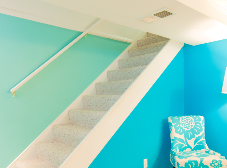 A carpeted staircase with a white handrail sits between walls painted in light mint and bright turquoise.