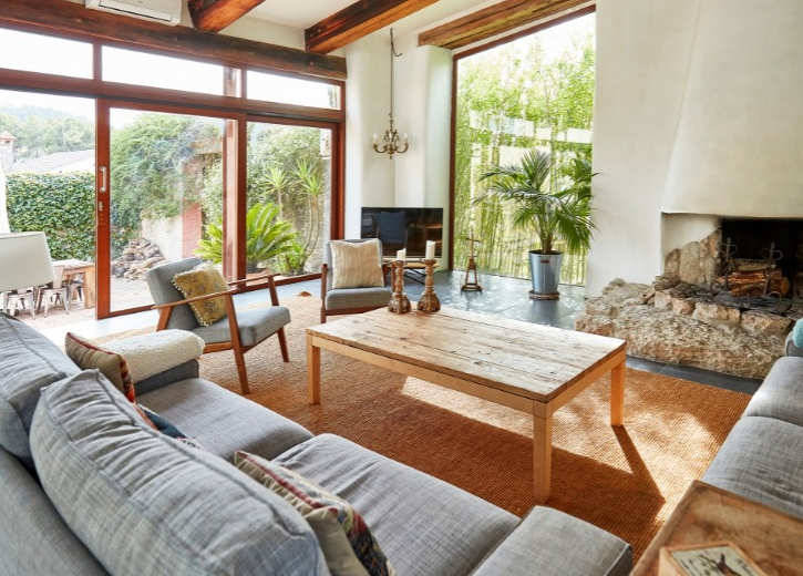 A sunlit, modern living room with gray sofas, a wood coffee table, two armchairs, and a stone fireplace.