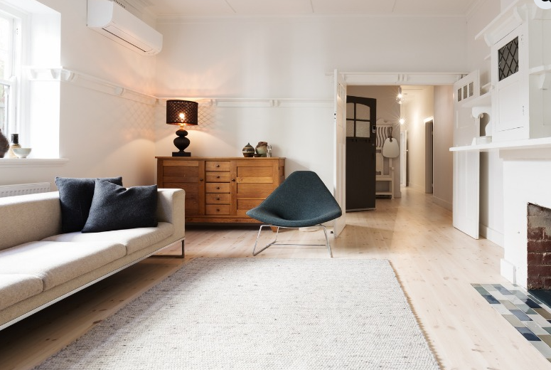 Modern, minimalist living room with a cream sofa, grey lounge chair, wooden dresser, and white walls.