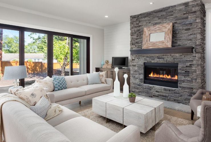 A modern living room with a stone fireplace, light-colored sofas, a white square coffee table, and large patio doors.