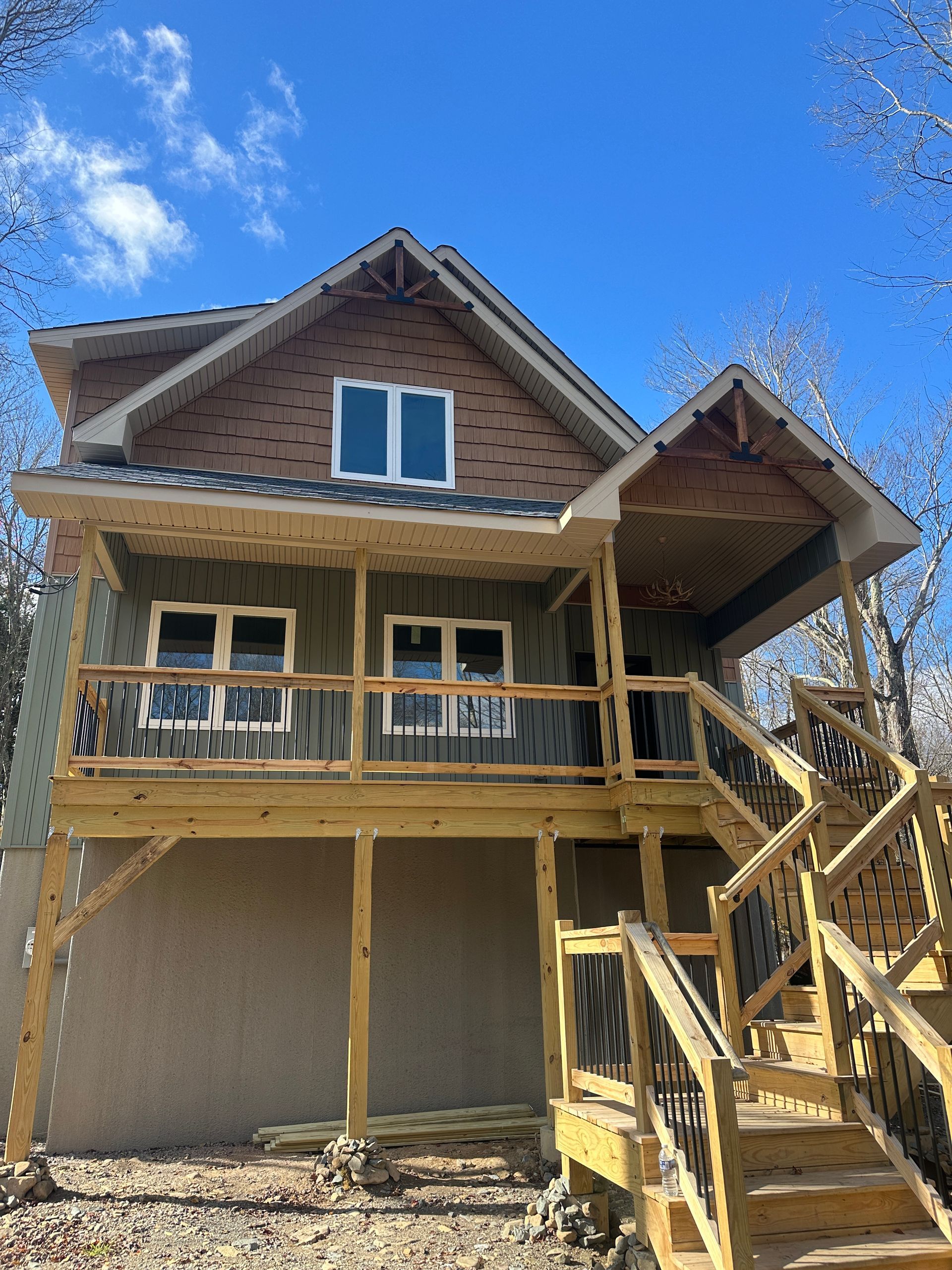 A two-story house under construction with wood framing, a partially finished exterior, and a new wooden deck and stairs.