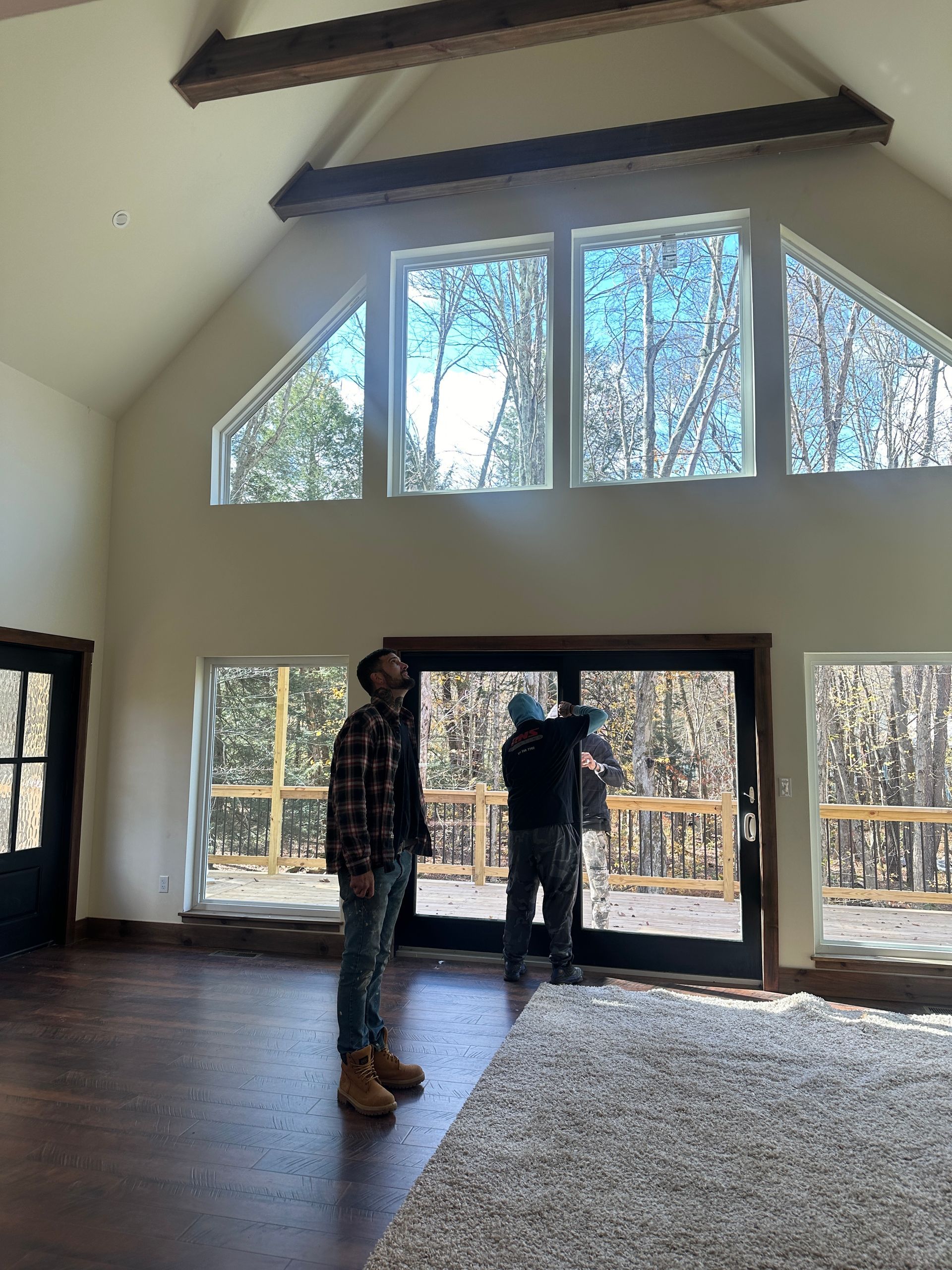 Two workers stand in a modern, high-ceilinged room with large windows and wooden beams, finishing a sliding glass door.