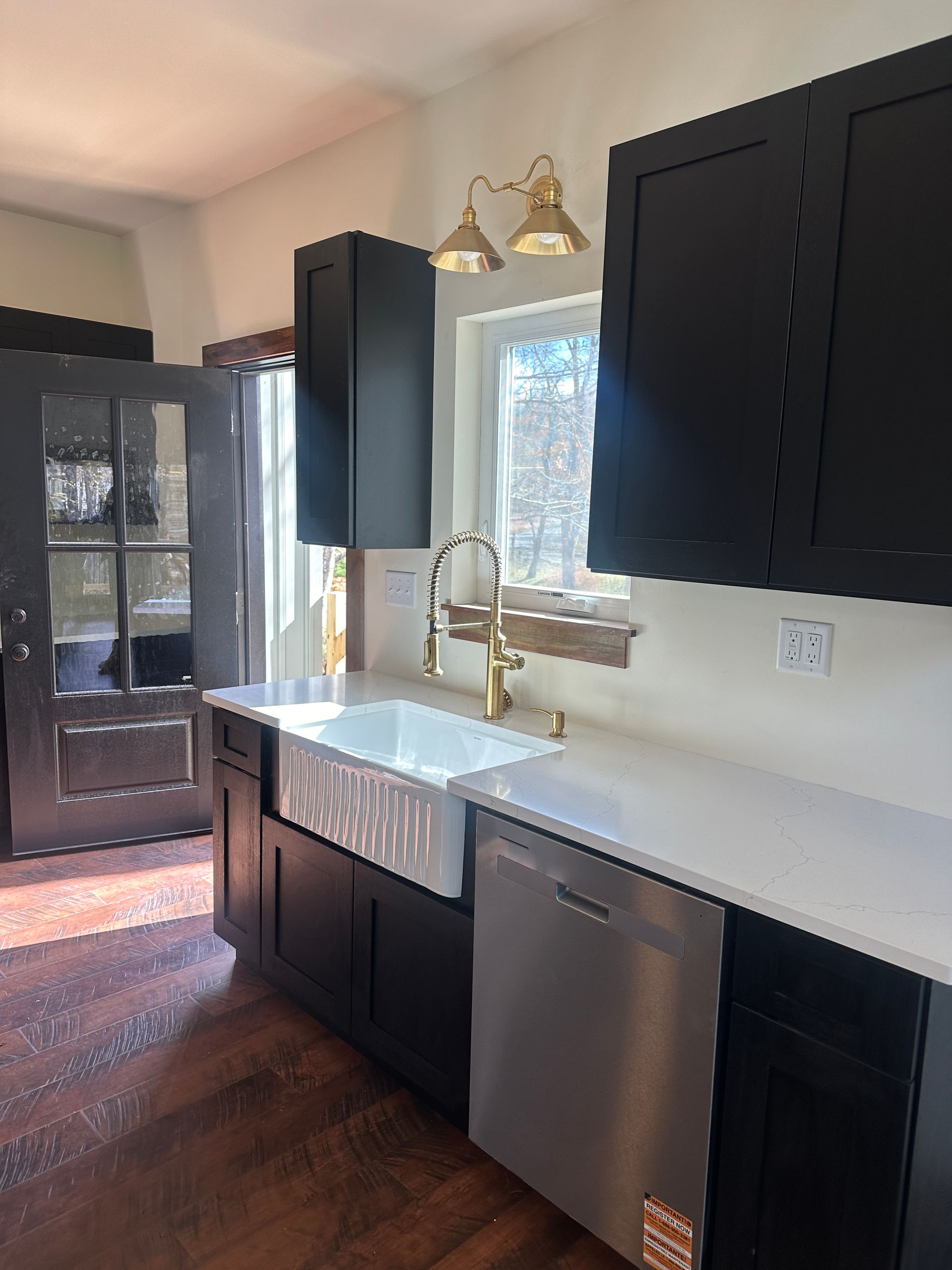 Modern kitchen with black cabinets, white countertops, a farmhouse sink, and gold hardware by a sunlit window.
