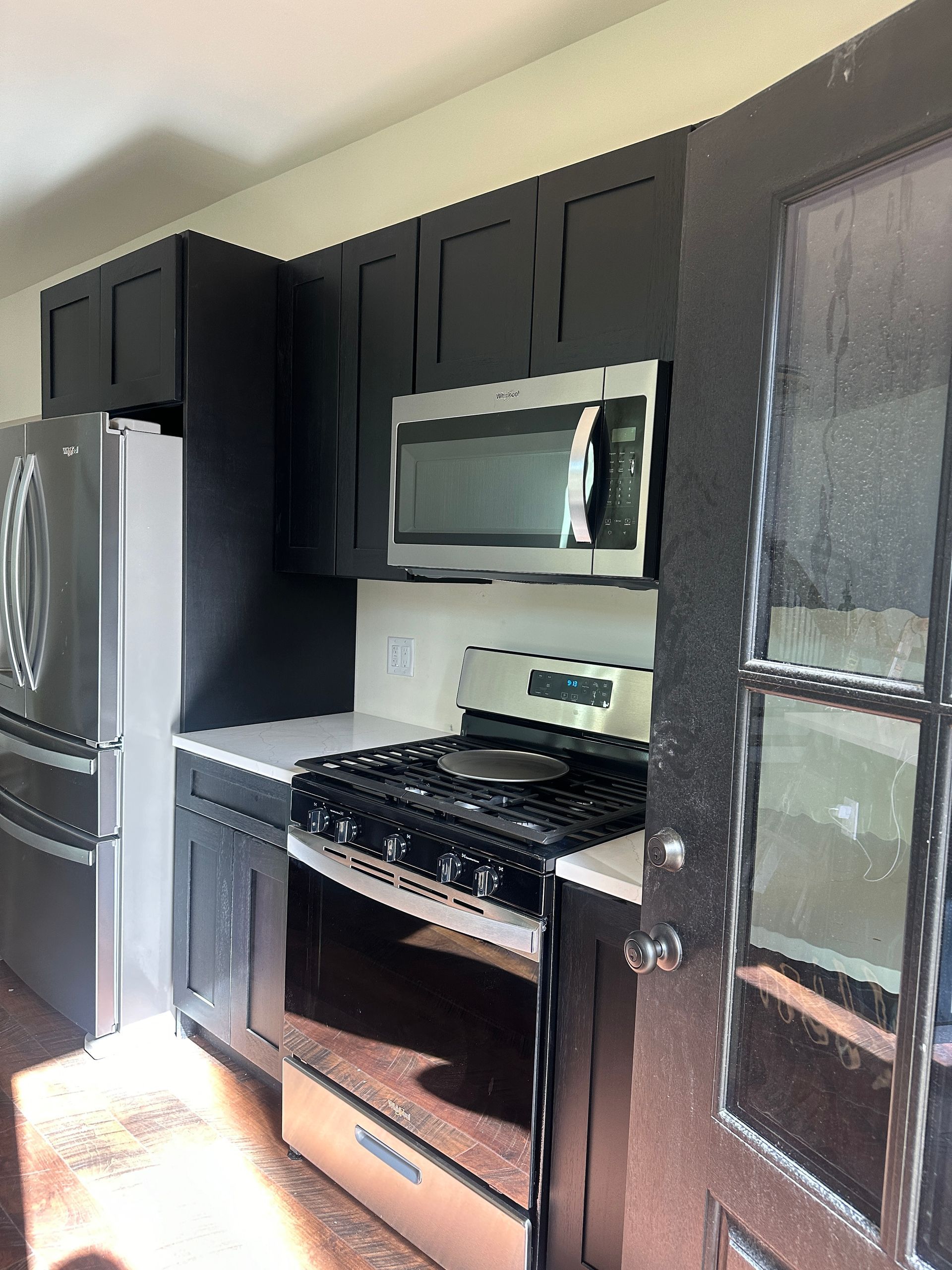 A kitchen featuring black cabinets, stainless steel appliances, white countertops, and a glass-paned door.