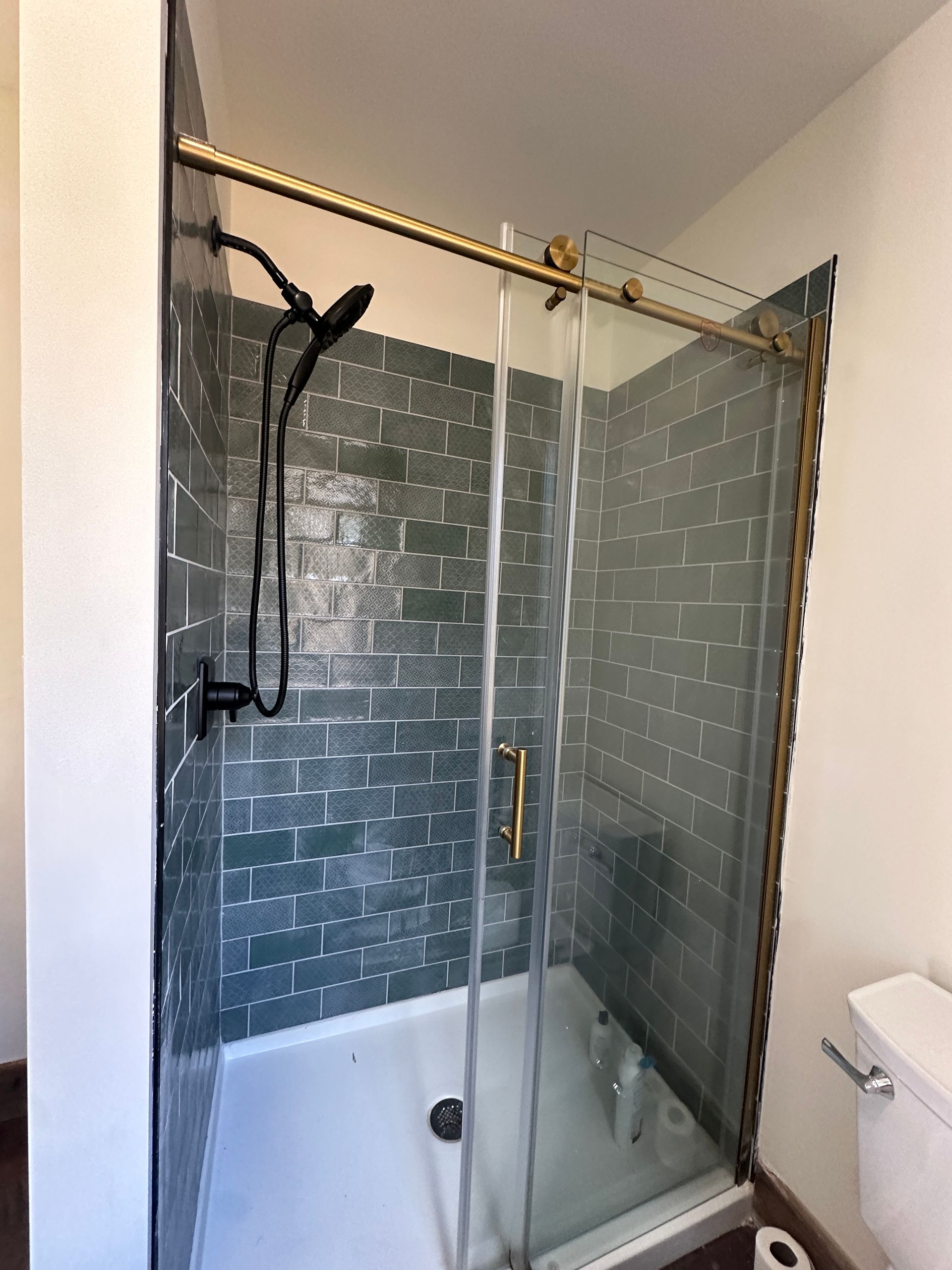 A walk-in shower with dark gray subway tile walls, a white base, a glass door, and brass hardware in a bathroom.