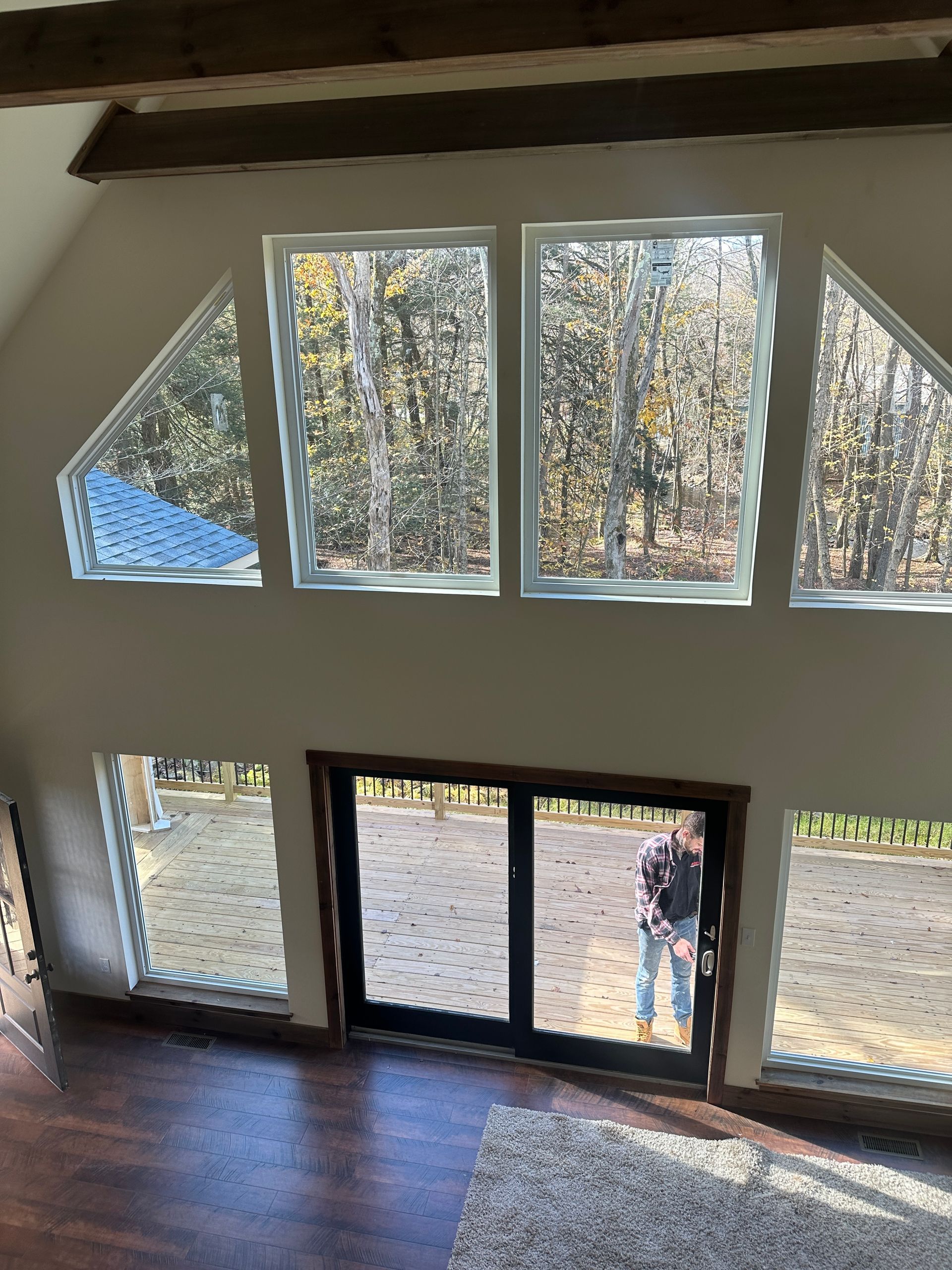 High-angle view of a living room with tall, multi-pane windows and a double door looking out onto a wooded area.