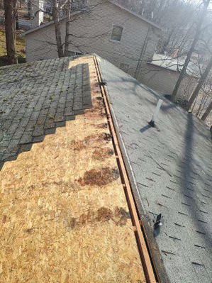 A section of a roof under repair, showing exposed plywood decking next to existing shingles and a roof vent pipe.