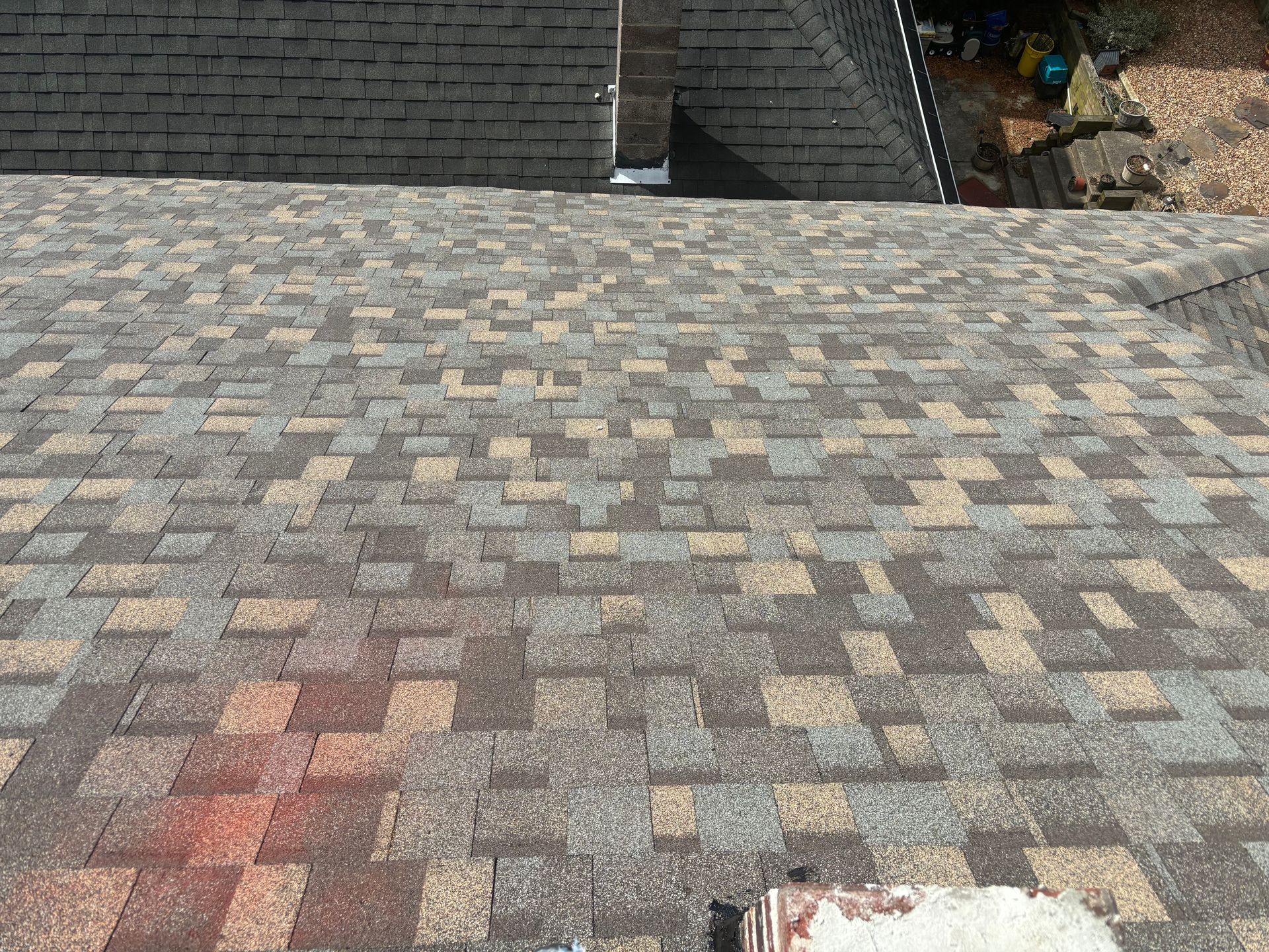 A high-angle view of a multi-colored architectural shingle roof with a chimney in the foreground.