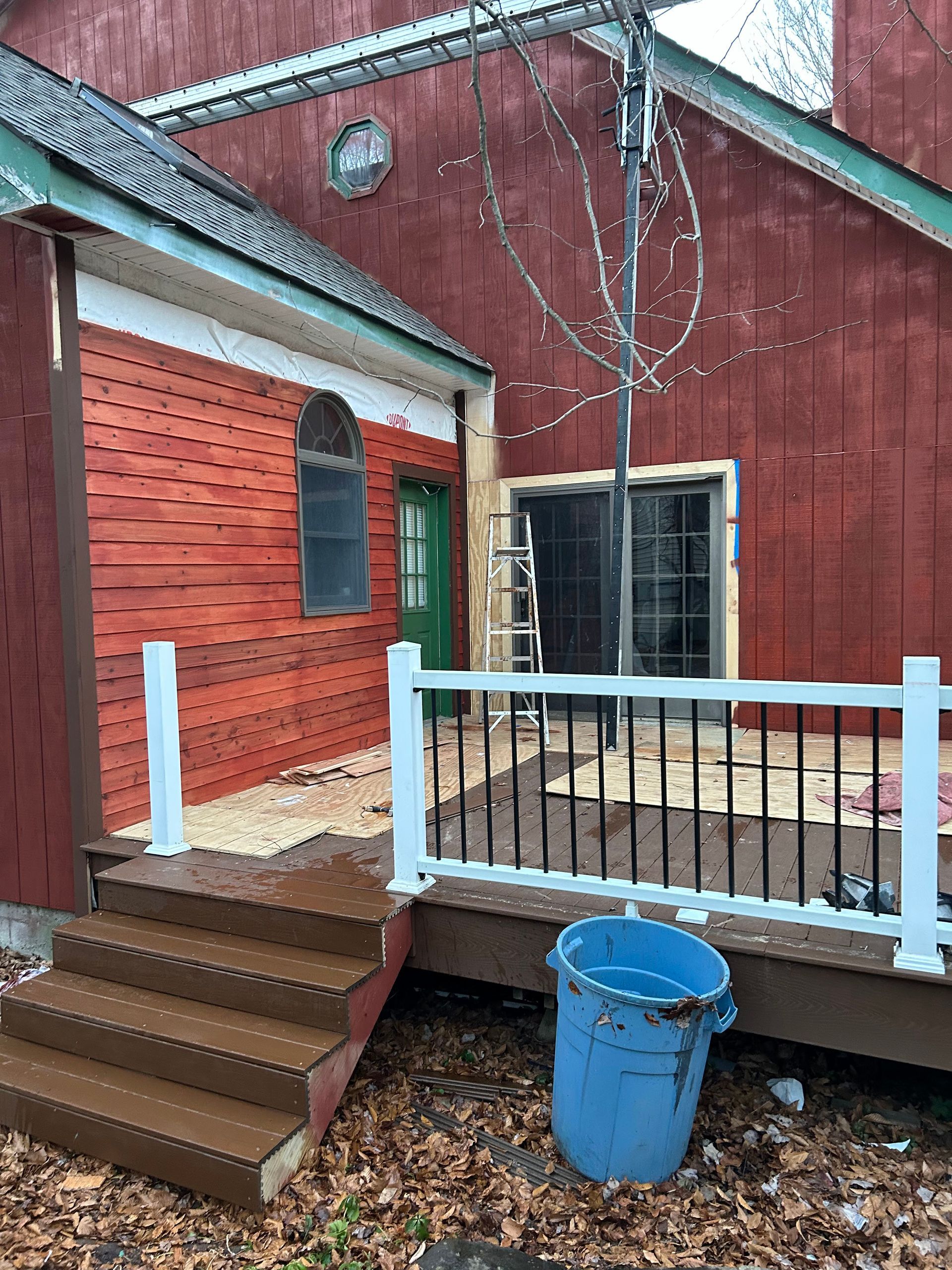 A red barn-style building with a new wooden deck, green door, and blue trash can in the foreground.